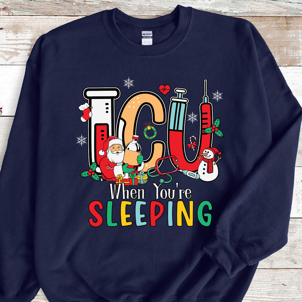 May include: Navy blue sweatshirt with a colorful graphic. The graphic features the letters "ICU" in orange and red, with medical and Christmas-themed illustrations. Text below reads "When You're SLEEPING".