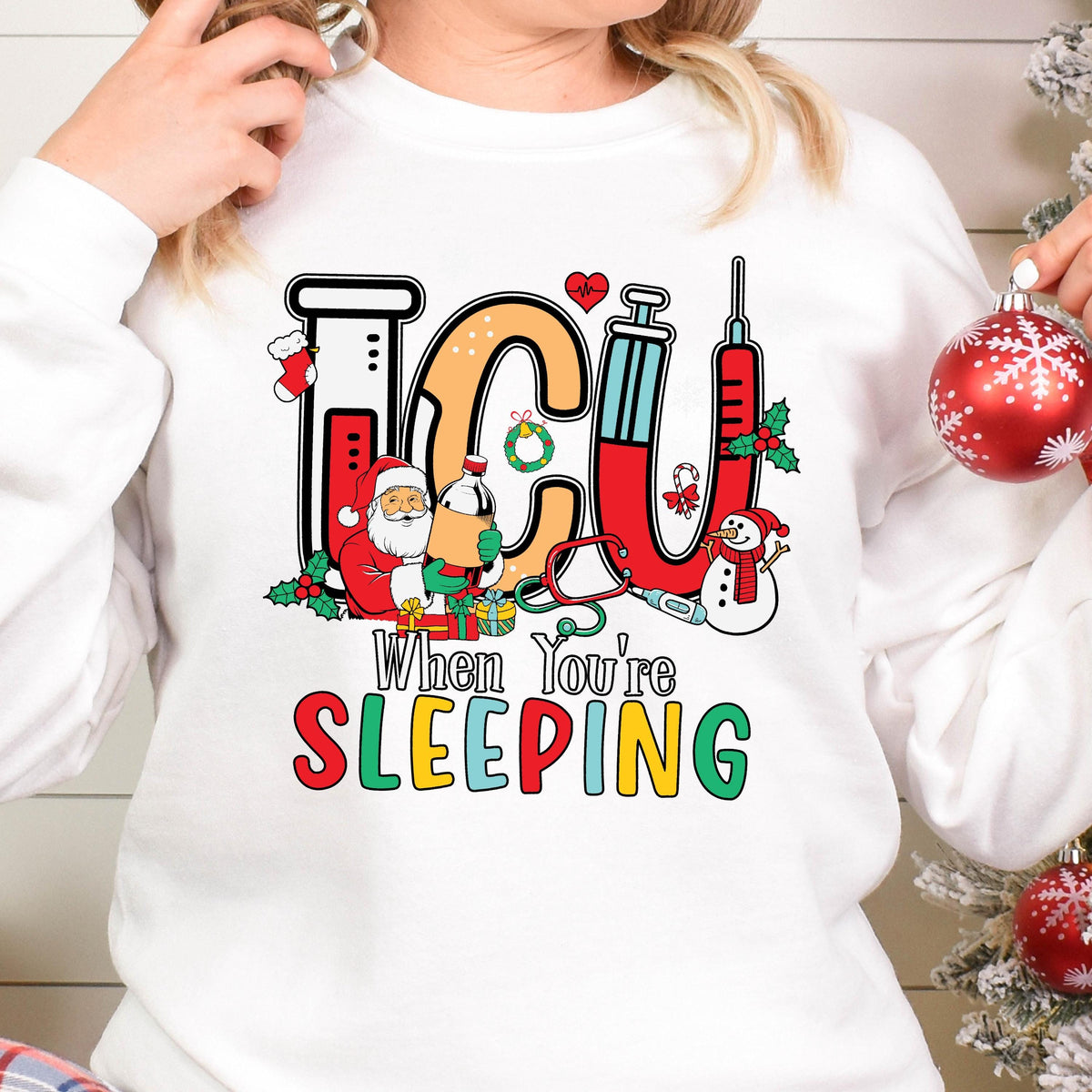 May include: White sweatshirt with a colorful graphic design featuring the letters "ICU" in orange, red, and blue, along with Christmas-themed illustrations. The text "When You're SLEEPING" is below the graphic.