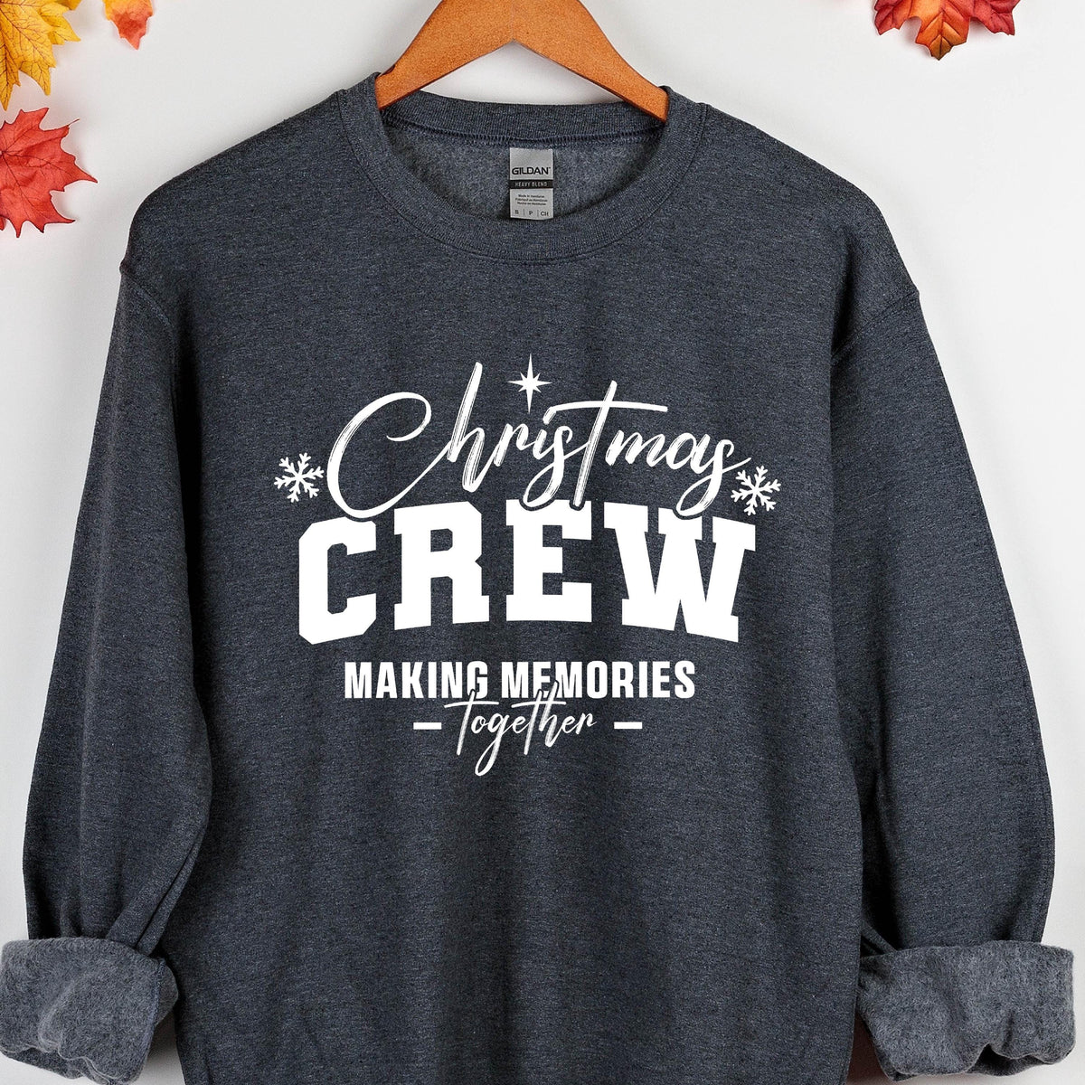 May include: A dark charcoal gray crewneck sweatshirt featuring white screen-printed text that reads Christmas CREW MAKING MEMORIES Together, accented with small white snowflake icons and a star symbol above the word Christmas.