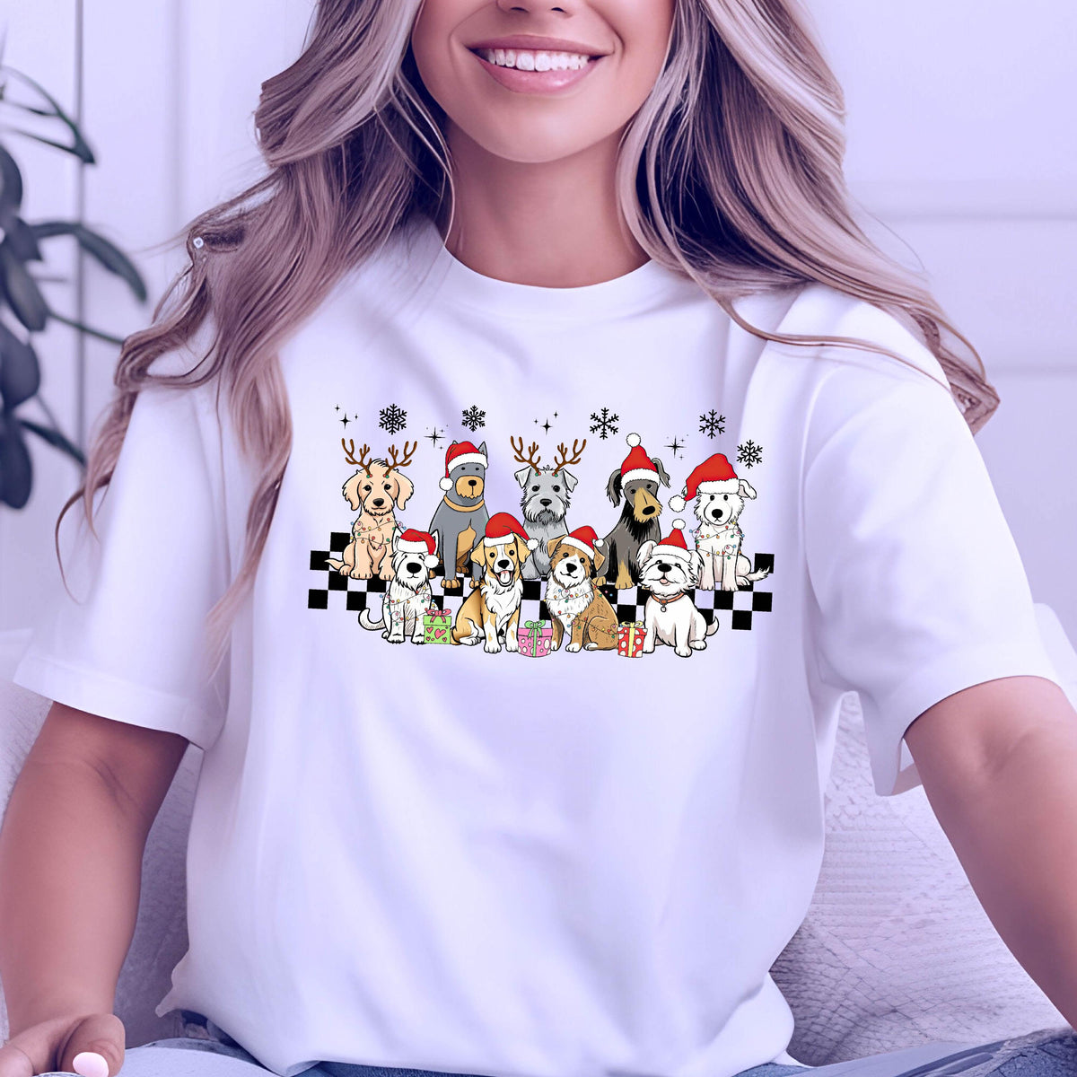 May include: White t-shirt featuring a festive graphic of various dog breeds wearing Santa hats and reindeer antlers. The dogs are arranged on a black and white checkered pattern, with snowflakes and gifts. A cheerful holiday-themed design.