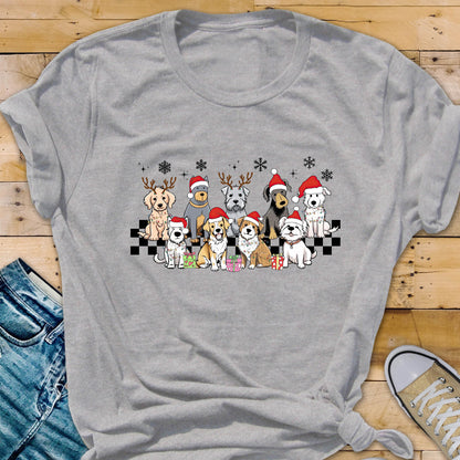 May include: A gray t-shirt featuring a festive design of various dog breeds wearing Santa hats and reindeer antlers. The dogs are arranged on a black and white checkered pattern, with snowflakes above them. A fun, holiday-themed graphic tee.