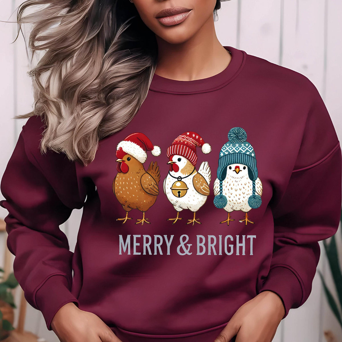 May include: A maroon sweatshirt with a Christmas-themed design featuring three chickens wearing festive hats. The chickens are brown, white, and white with blue accents. The text "Merry & Bright" is printed below the chickens.