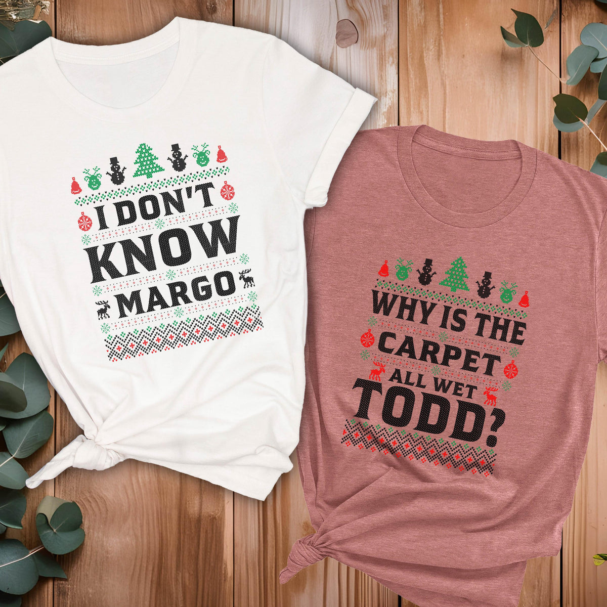 May include: Two short-sleeved t-shirts with Christmas-themed designs. One is white with the text "I DON'T KNOW MARGO" and the other is mauve with the text "WHY IS THE CARPET ALL WET TODD?". Both shirts have festive graphics.