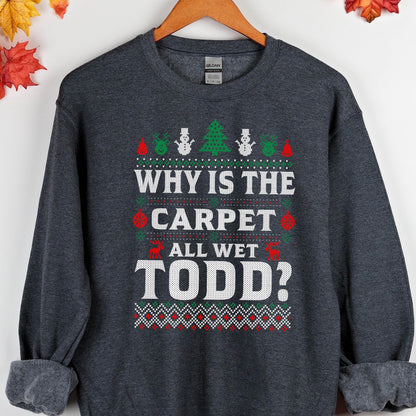 May include: A dark gray sweatshirt with a Christmas-themed design. The design features a white text that reads "Why is the carpet all wet Todd?" with a green and red pattern around the text.