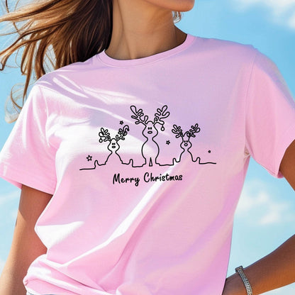 May include: A light pink t-shirt featuring a black line drawing of three reindeer with antlers and stars. The words "Merry Christmas" are written in a script font below the reindeer. The shirt is made of a soft material.