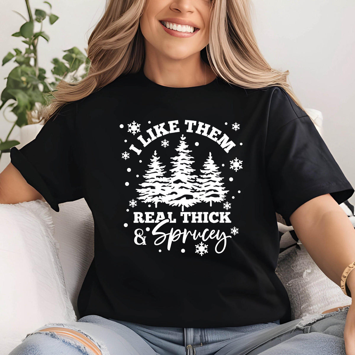 May include: Black t-shirt with a white graphic design featuring three stylized pine trees and the text "I LIKE THEM REAL THICK & SPRUCEY" in a playful font, surrounded by snowflakes. The shirt has short sleeves.