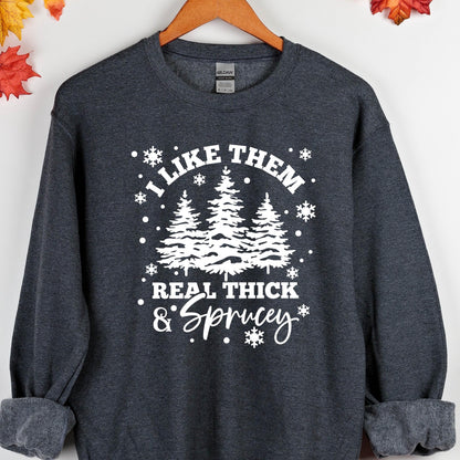 May include: A dark heather gray crewneck sweatshirt featuring a white graphic print of three pine trees surrounded by snowflakes. The text reads I LIKE THEM REAL THICK & SPRUCEY in a mix of bold block lettering and a cursive script font.