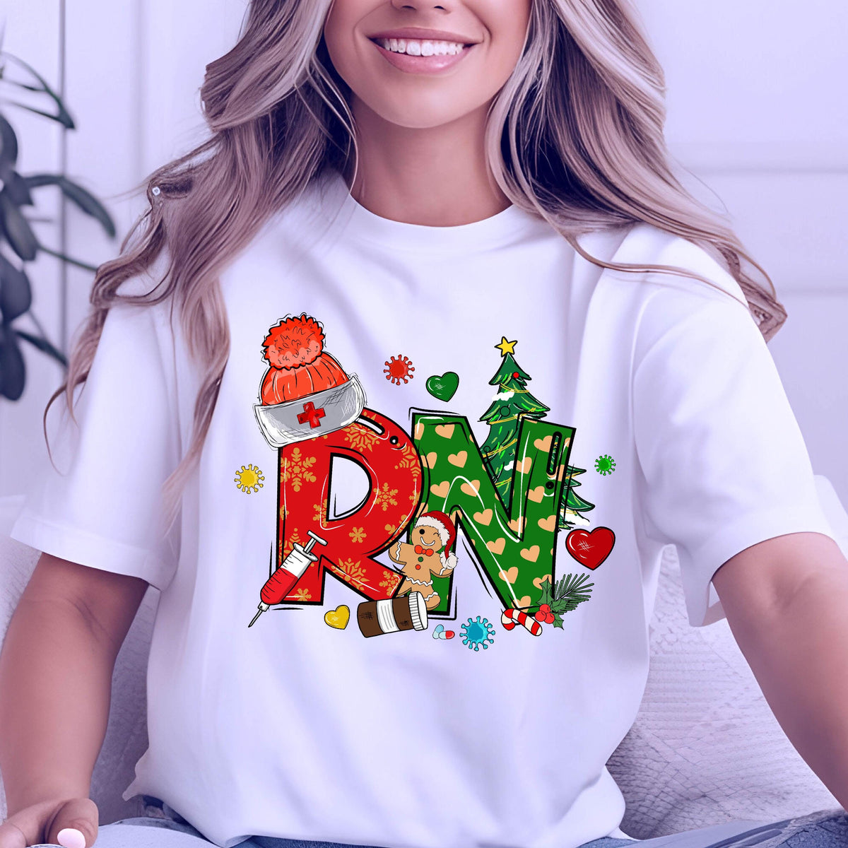 May include: White t-shirt with a colorful graphic design featuring the letters "RN" in red and green, decorated with Christmas-themed elements like a Santa hat, gingerbread man, and Christmas tree.
