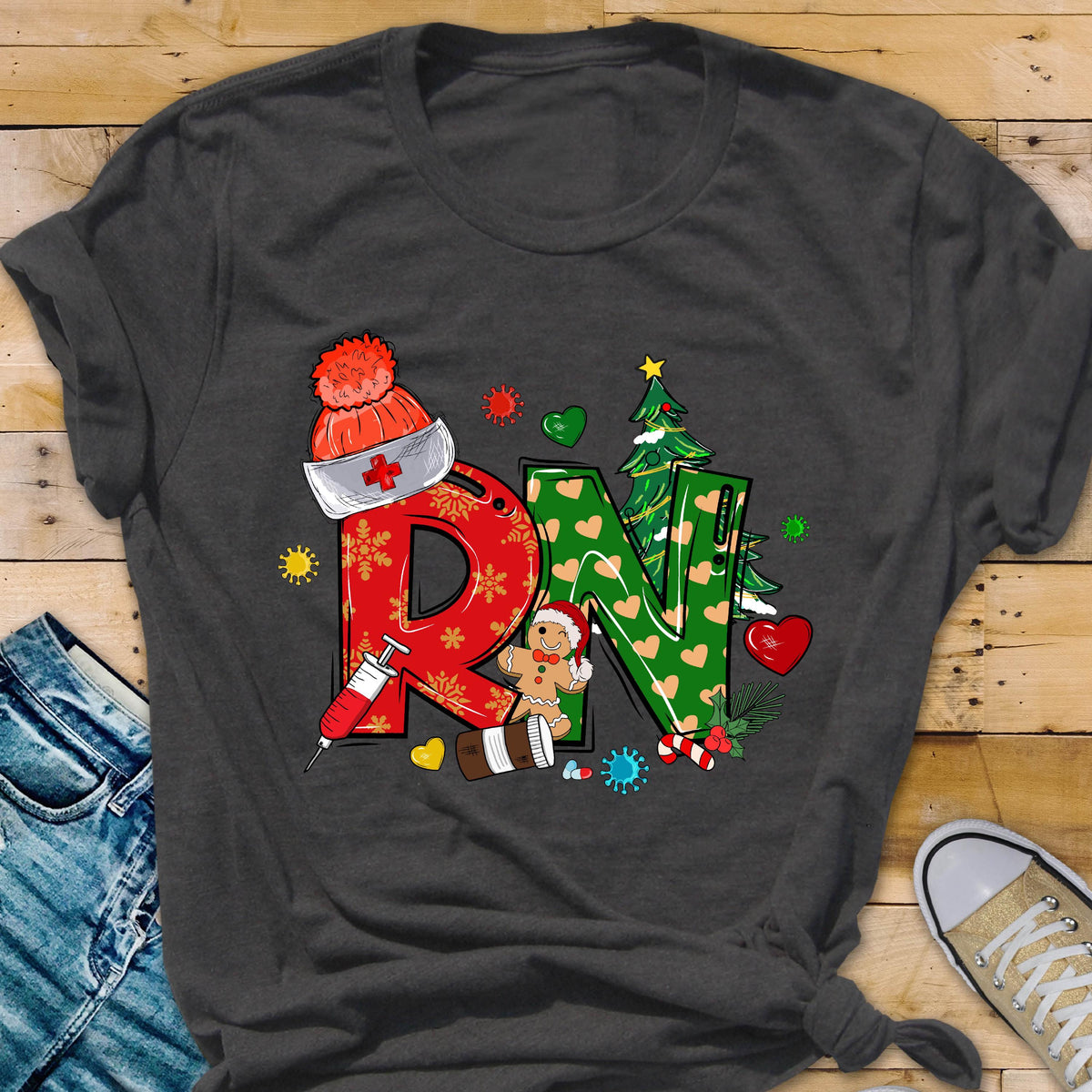 May include: Dark gray t-shirt featuring a festive design with the letters "RN" in red and green, decorated with Christmas elements. Includes a syringe, gingerbread person, and a nurse's hat with a cross.
