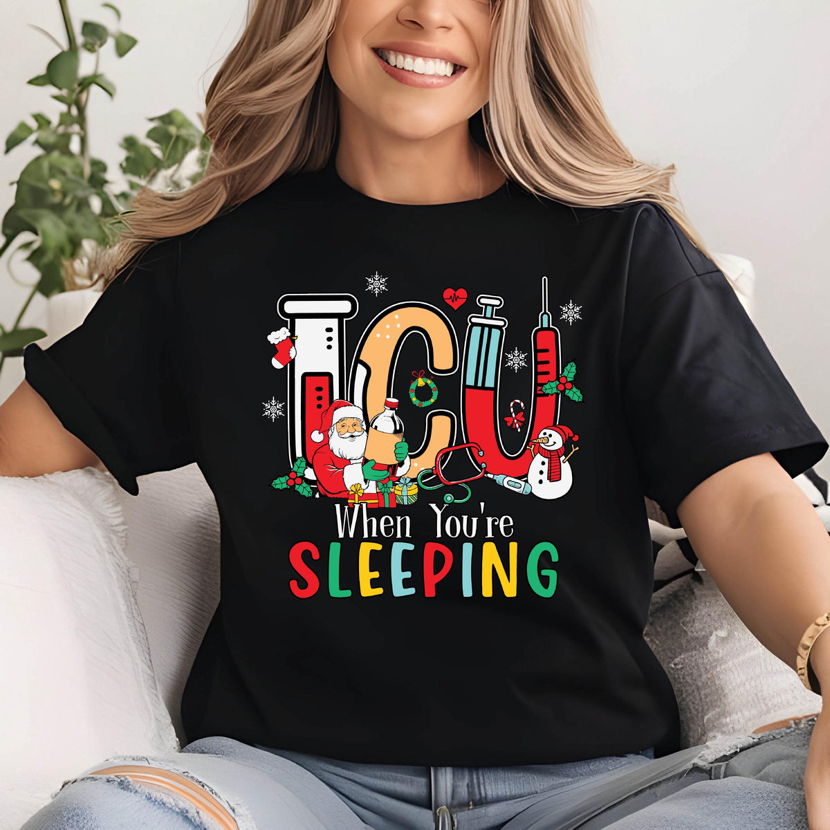 May include: Black t-shirt with a colorful graphic design featuring the letters "ICU" in orange, red, and white, along with medical equipment and Christmas-themed characters. The text "When You're Sleeping" is below the graphic.