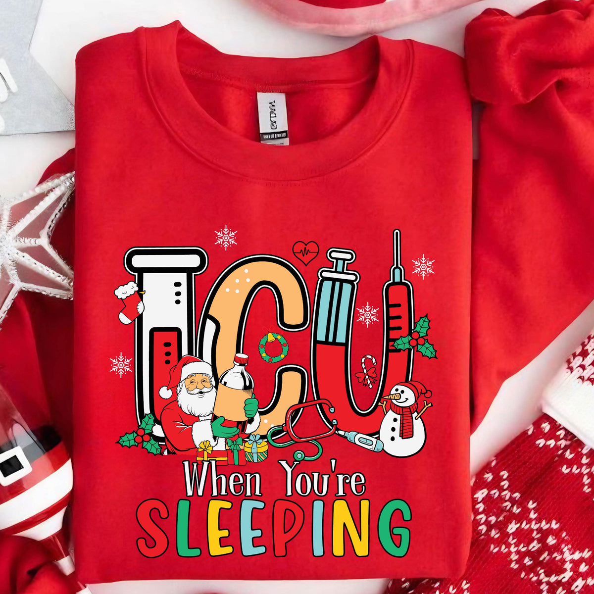 May include: A red sweatshirt with the text "ICU When You're Sleeping" in colorful letters. The design includes medical symbols, snowflakes, Santa Claus, and a snowman, all in a festive Christmas theme.