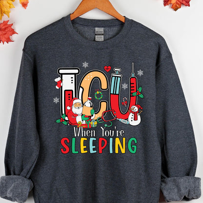 May include: Dark gray sweatshirt with a colorful graphic. The graphic features the letters "ICU" in orange and red, along with Santa Claus, a snowman, and medical equipment. The text "When You're SLEEPING" is below the graphic.