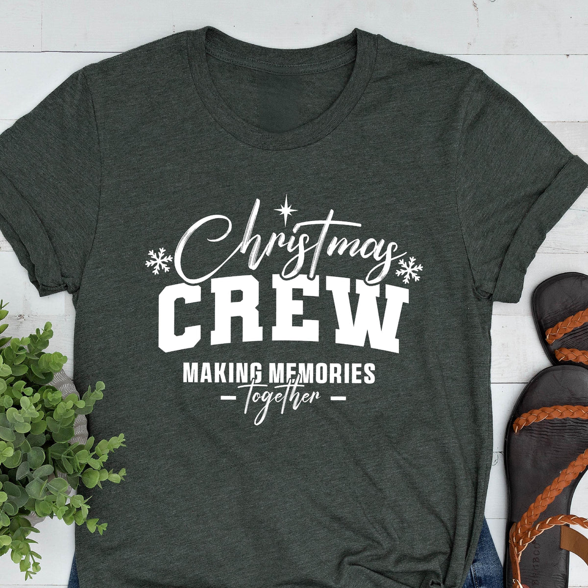 May include: A dark charcoal gray short-sleeve t-shirt featuring white screen-printed text that reads Christmas CREW MAKING MEMORIES Together, accented with small white snowflake icons and a star symbol above the word Christmas.