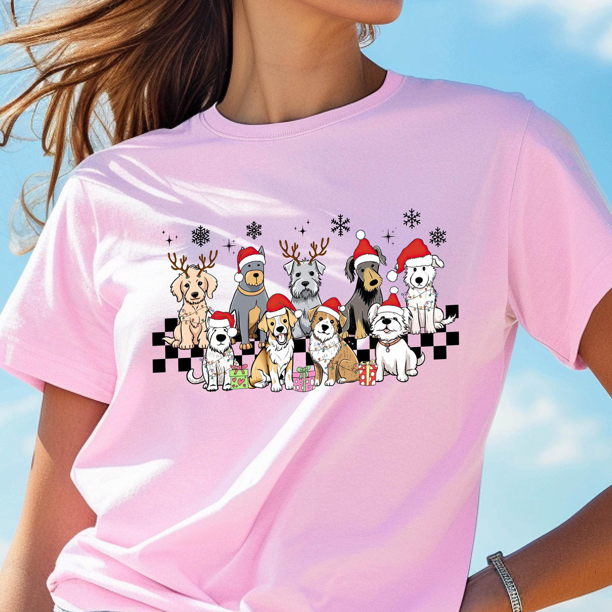 May include: Pink t-shirt featuring a festive graphic of various dog breeds wearing Santa hats and reindeer antlers. The dogs are arranged on a black and white checkered pattern, with snowflakes and presents. A fun, holiday-themed tee.