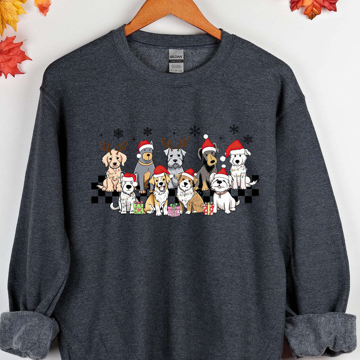 May include: Dark gray sweatshirt featuring a festive graphic of various dog breeds wearing Santa hats and reindeer antlers. The dogs are arranged in a row with snowflakes above and gifts below, creating a holiday theme. The sweatshirt has a crew neck and long sleeves.