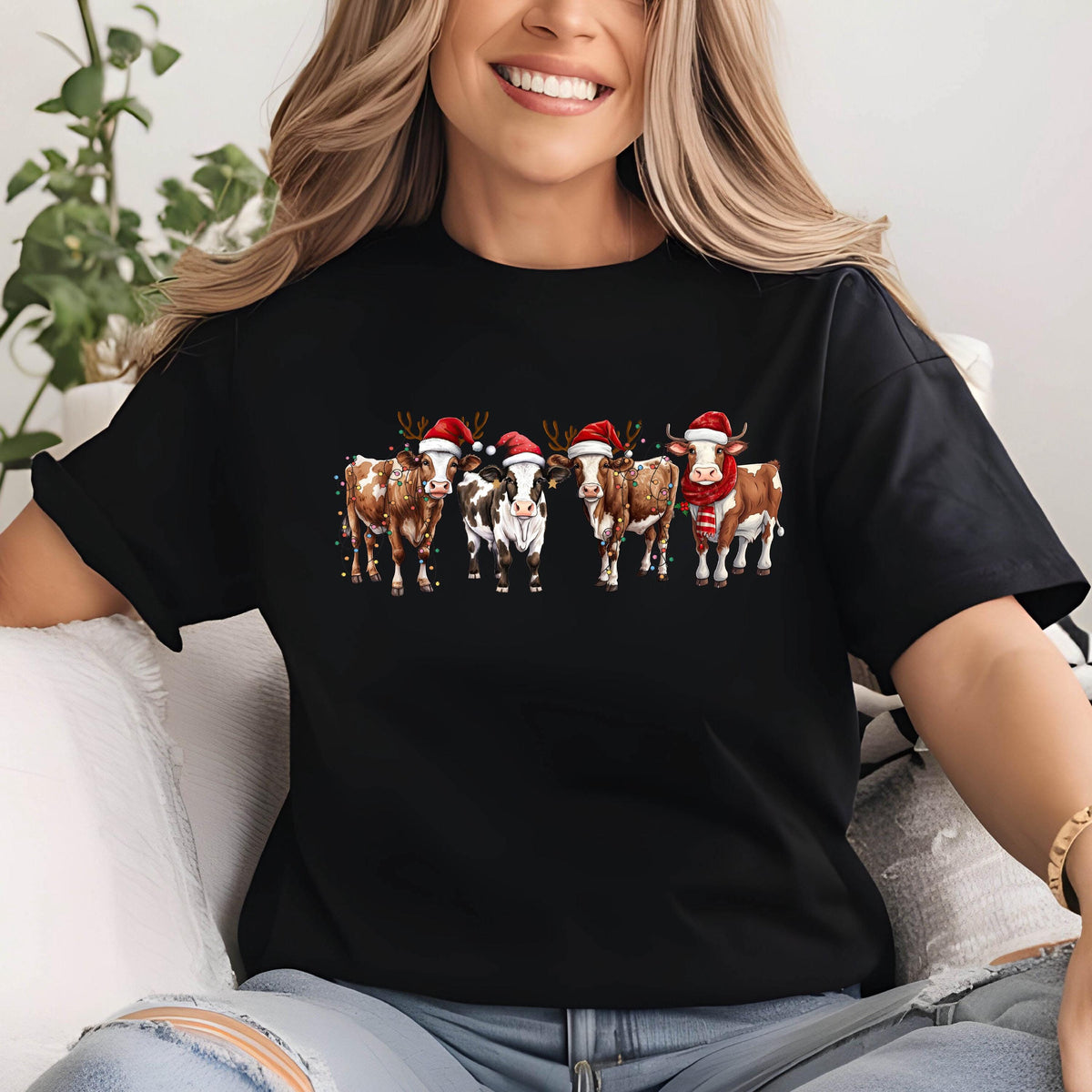 May include: Black t-shirt featuring a festive graphic of five cows adorned with Santa hats, reindeer antlers, and a scarf. The cows are brown, white, and black, with string lights. A fun, holiday-themed design.