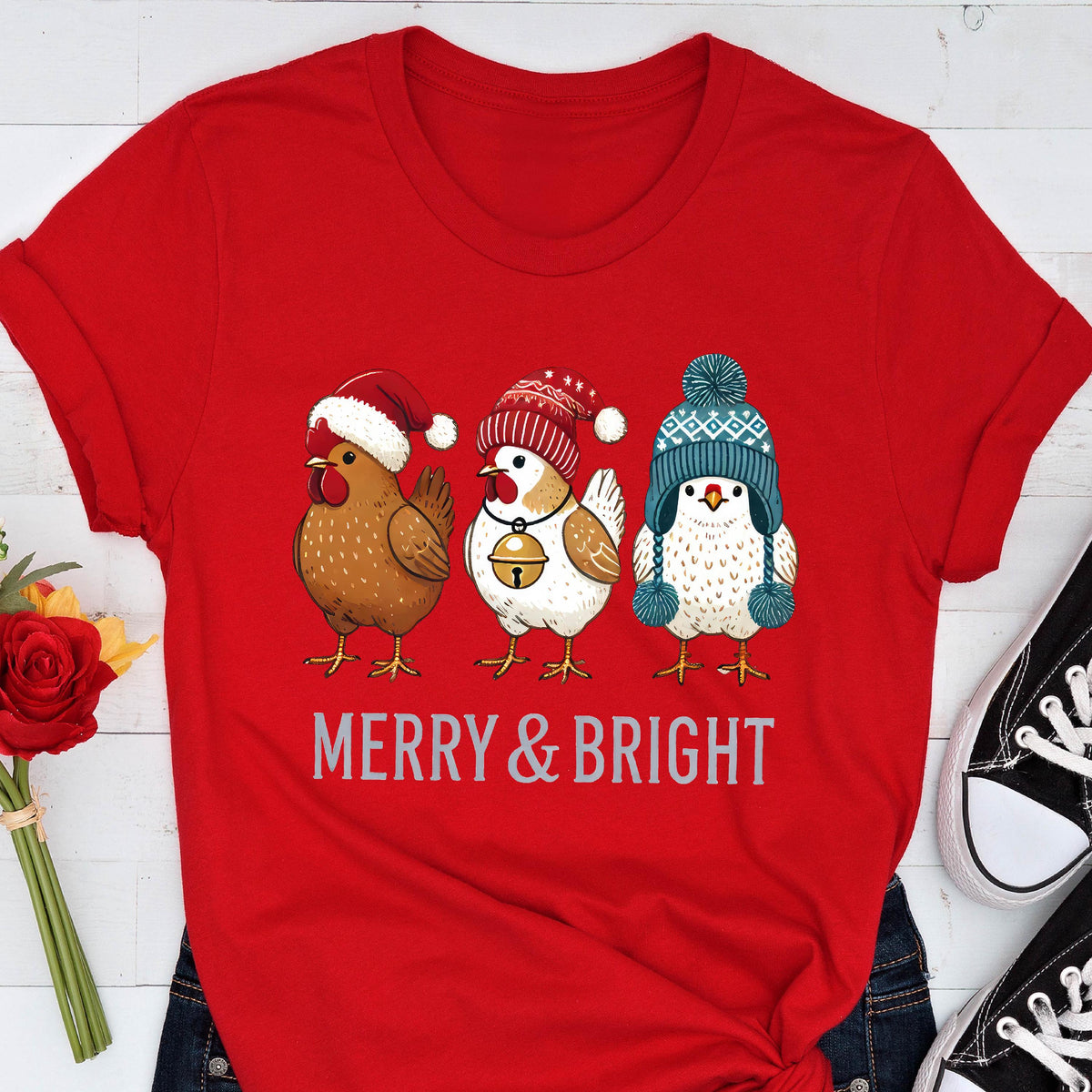 May include: Red t-shirt featuring three cartoon chickens wearing winter hats. The chickens are brown, white, and white with a blue hat. The text "MERRY & BRIGHT" is printed below the chickens in a silver color.