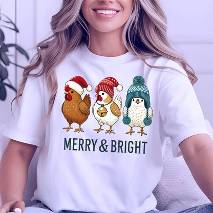 May include: White t-shirt featuring three cartoon chickens wearing festive winter hats. The chickens are brown, white, and beige, with red and blue hats. The text "MERRY & BRIGHT" is printed below the chickens in green.
