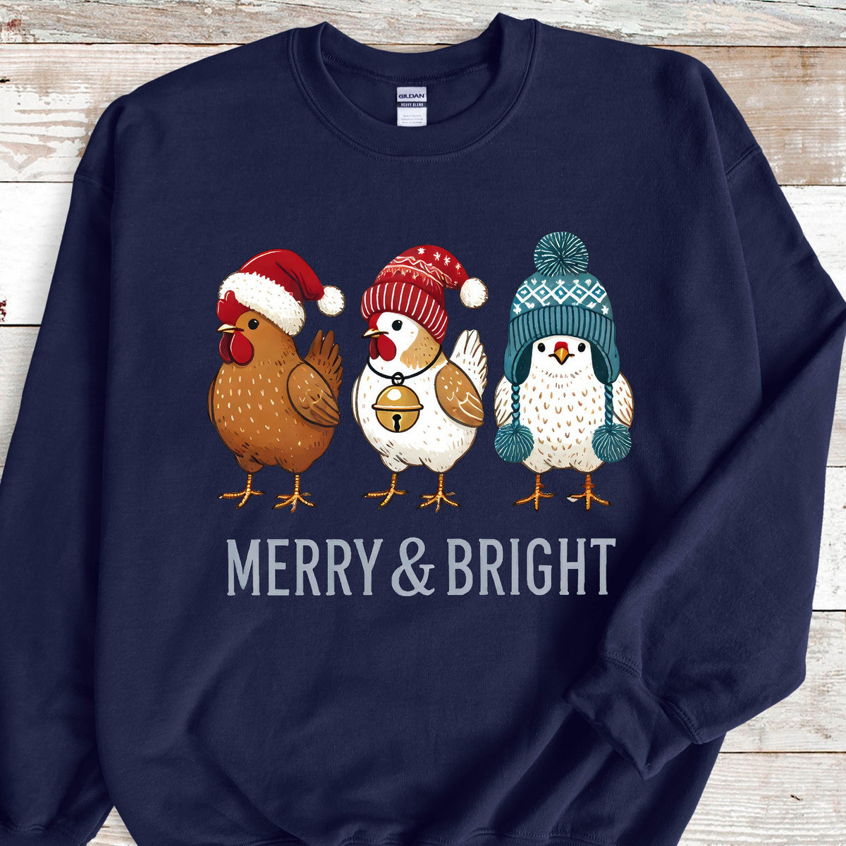 May include: A navy blue sweatshirt with a Christmas-themed design featuring three chickens wearing festive hats. The chickens are wearing a red Santa hat, a red and white Santa hat, and a blue and white knit hat. The text "Merry & Bright" is printed below the chickens.
