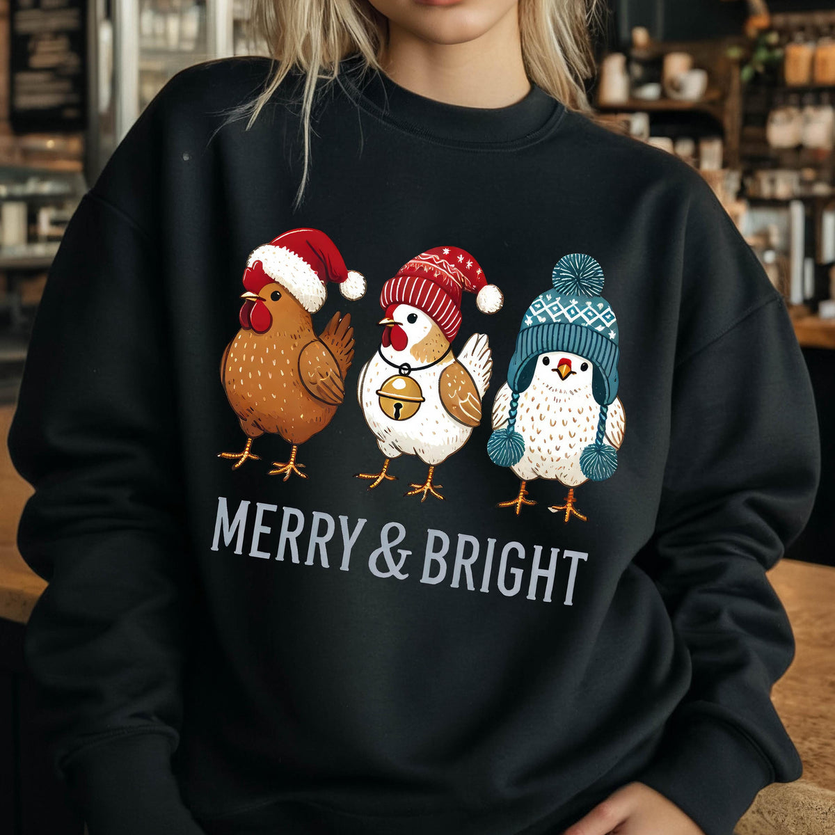 May include: Black sweatshirt with a festive design featuring three chickens wearing winter hats. The chickens are wearing a red and white Santa hat, a red and white stocking cap, and a blue and white knit hat. The text "Merry & Bright" is printed below the chickens.