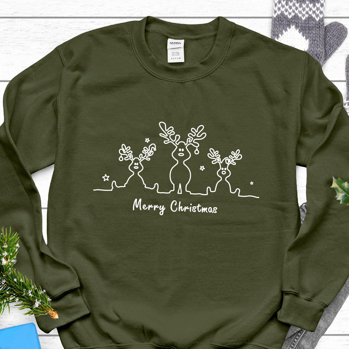 May include: An olive green crewneck sweatshirt featuring a white line art graphic of three reindeer with antlers and the text Merry Christmas centered below the figures. The design is printed on the front of the long-sleeved pullover garment.