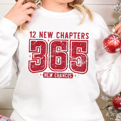 May include: White sweatshirt with the text "12 New Chapters 365 New Chances" in distressed red lettering. The design features the numbers "365" prominently displayed, with the words "New Chapters" above and "New Chances" below.