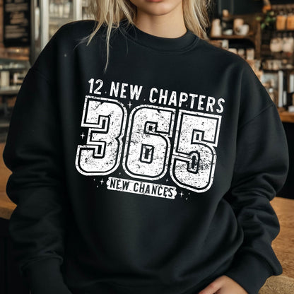 May include: Black sweatshirt with the text "12 NEW CHAPTERS 365 NEW CHANCES" in distressed white lettering. The sweatshirt is a crew neck style, perfect for casual wear. The design is centered on the front of the garment.