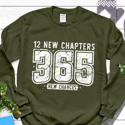 May include: An olive green sweatshirt with the text "12 NEW CHAPTERS 365 NEW CHANCES" in distressed white lettering. The sweatshirt has a crew neck and long sleeves. The design is centered on the front.