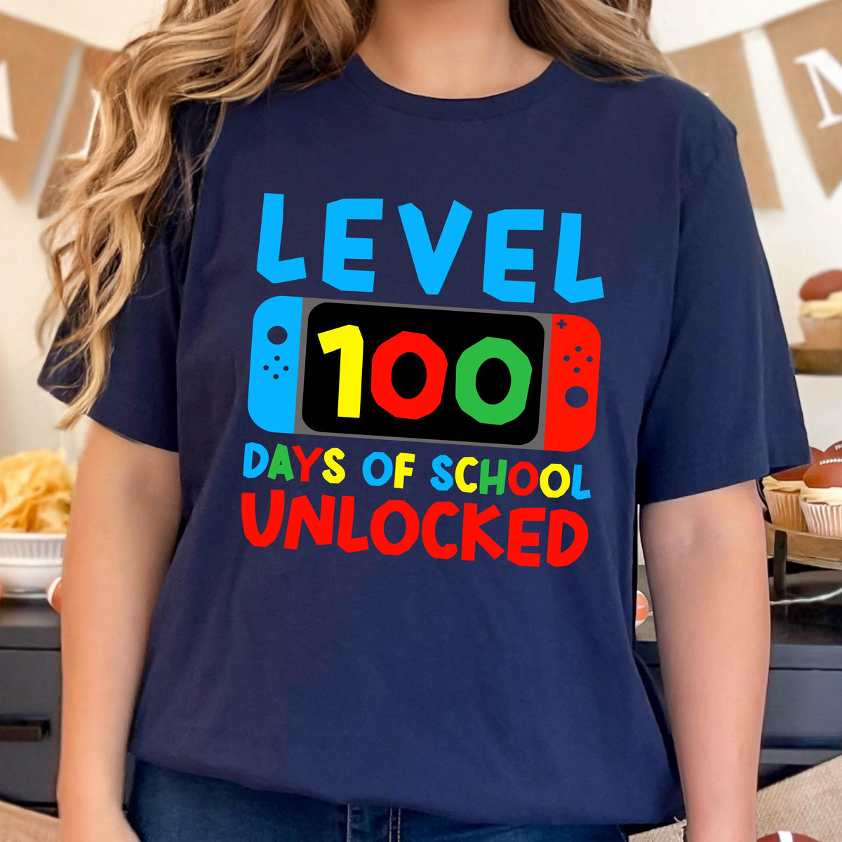 May include: A navy blue t-shirt with the text "LEVEL 100 DAYS OF SCHOOL UNLOCKED" in colorful letters. The text is stylized to look like a video game console.