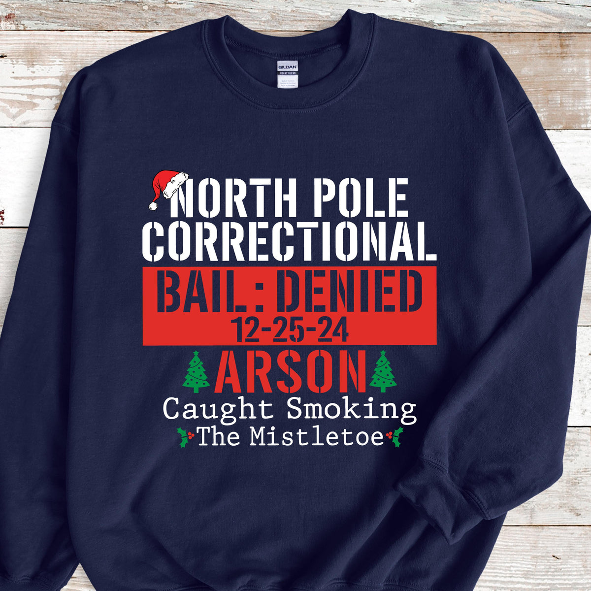 May include: Navy blue sweatshirt with the text "NORTH POLE CORRECTIONAL BAIL: DENIED 12-25-24 ARSON Caught Smoking The Mistletoe" in white and red. A Santa hat graphic is above the text.