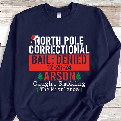 May include: Navy blue sweatshirt with the text "NORTH POLE CORRECTIONAL BAIL: DENIED 12-25-24 ARSON Caught Smoking The Mistletoe" in white and red. A Santa hat graphic is above the text.