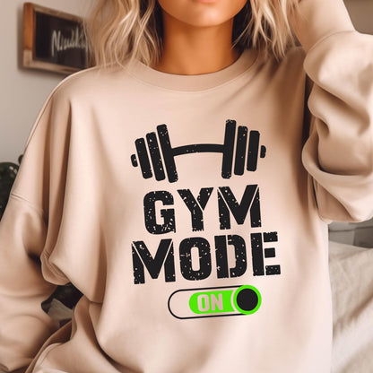 May include: A beige crewneck sweatshirt featuring a black graphic of a barbell above the distressed black text "GYM MODE" and a horizontal toggle switch graphic with the word "ON" in white letters against a bright green background.