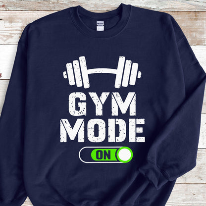 May include: A navy blue crewneck sweatshirt featuring a white graphic of a barbell above the distressed white text GYM MODE. Below the text is a white outlined toggle switch graphic with a bright green button containing the white text ON.