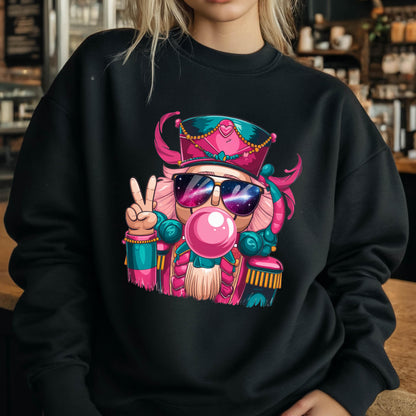May include: Black sweatshirt featuring a colorful illustration of a nutcracker wearing sunglasses and a pink hat. The nutcracker is blowing a bubblegum bubble and making a peace sign with its hand. The design has pink, teal, and gold accents.