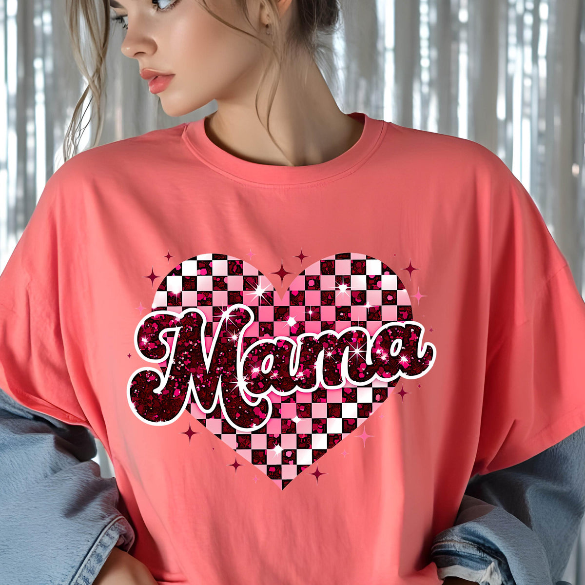May include: A pink t-shirt with a glittery pink and white checkered heart design and the word "Mama" in a glittery pink font.