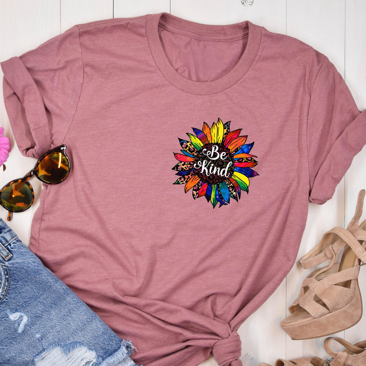 May include: A mauve t-shirt with a colorful sunflower graphic and the text "Be Kind" in white.