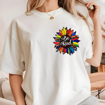 May include: White t-shirt featuring a colorful sunflower design with the words "Be Kind" in a script font. The sunflower has a rainbow of colors and a leopard print center. The shirt has short sleeves and a crew neck.