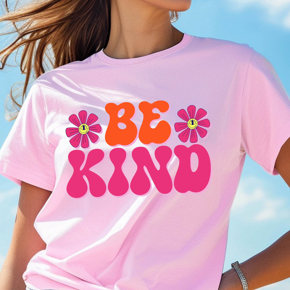 May include: Pink t-shirt with the text "BE KIND" in a retro font with pink and orange letters. The text is surrounded by two pink flowers with yellow smiley faces.