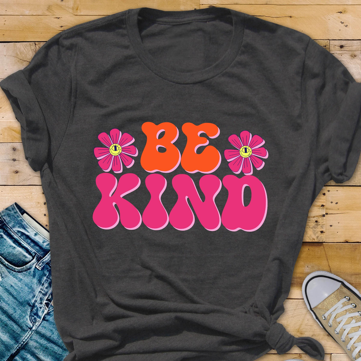 May include: A dark grey t-shirt with a pink and orange graphic that says "BE KIND" with two pink flowers with yellow smiley faces on them.