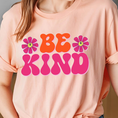 May include: A pink t-shirt with the words "BE KIND" in large, retro-style letters. The letters are pink and orange with a pink flower on each side.