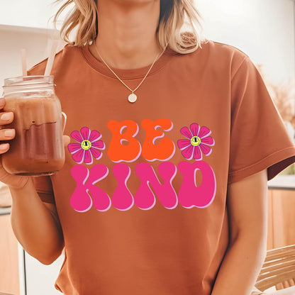 May include: A brown t-shirt with a pink and orange graphic that says "BE KIND" with two pink flowers with yellow smiley faces on them.