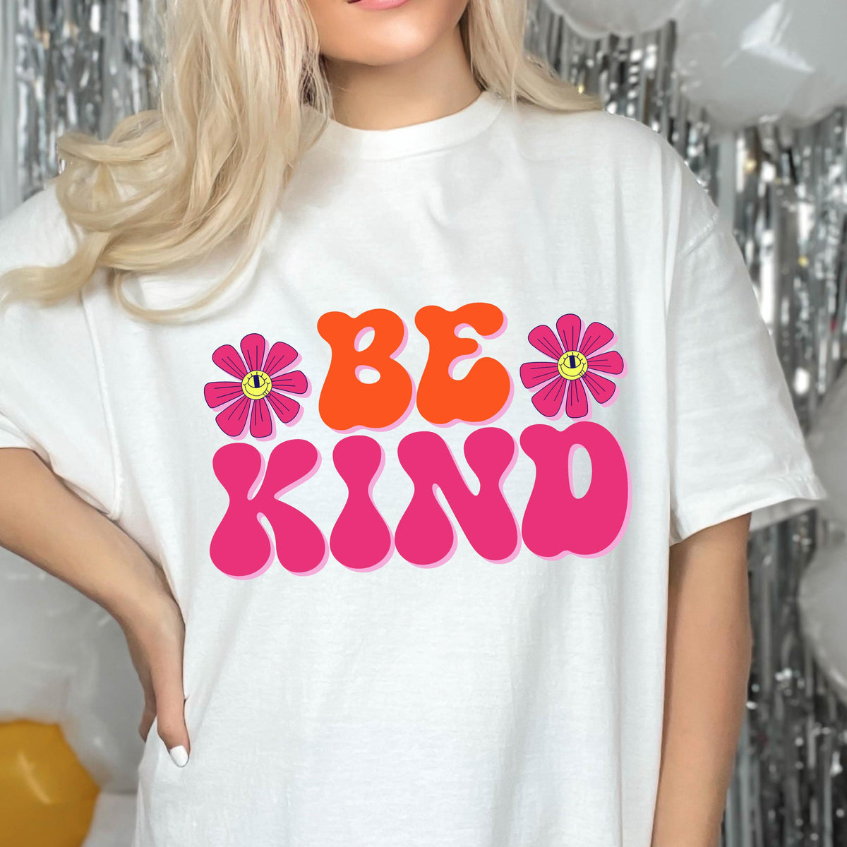 May include: White t-shirt with a pink and orange graphic that says "BE KIND" with two pink flowers with yellow smiley faces on them.