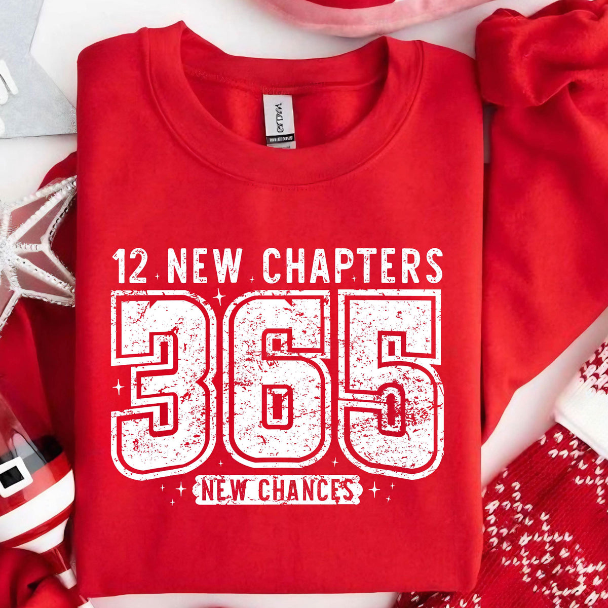 May include: A red sweatshirt with the text "12 NEW CHAPTERS 365 NEW CHANCES" in distressed white lettering. The sweatshirt is a crew neck style and appears to be made of a soft material. The design is centered on the front of the shirt.
