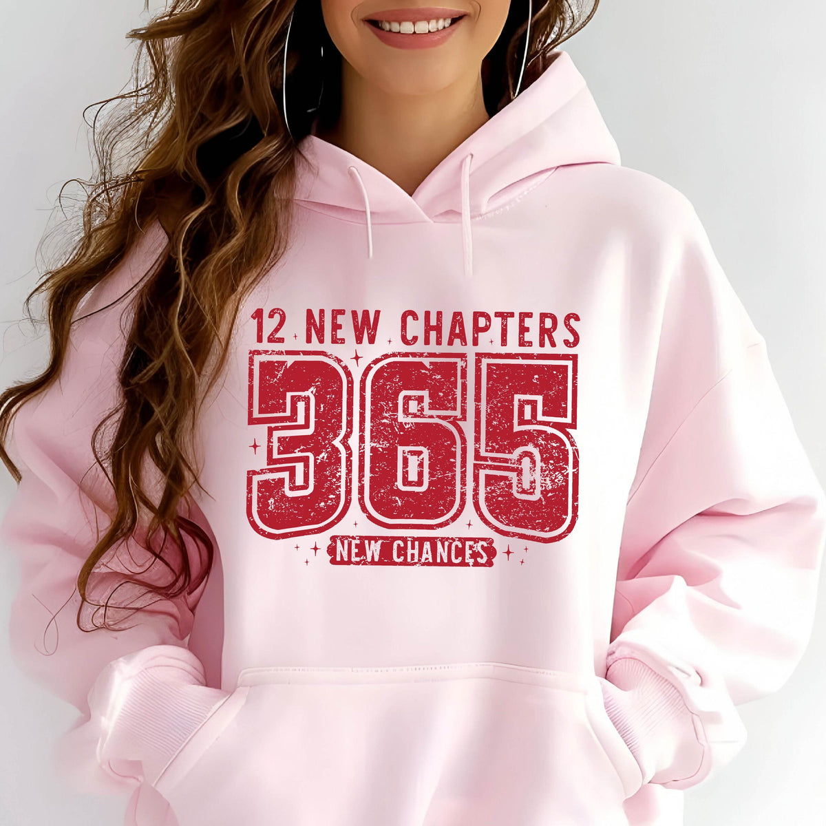 May include: A light pink hoodie with a red graphic that reads "12 NEW CHAPTERS 365 NEW CHANCES". The graphic has a distressed, vintage look. The hoodie has a drawstring hood and a front pocket.