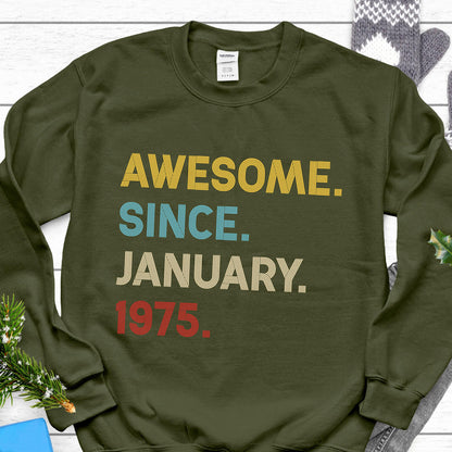 May include: An olive green sweatshirt with the text "AWESOME. SINCE. JANUARY. 1975." in yellow, blue, beige, and red. The sweatshirt is a casual garment, suitable for everyday wear.