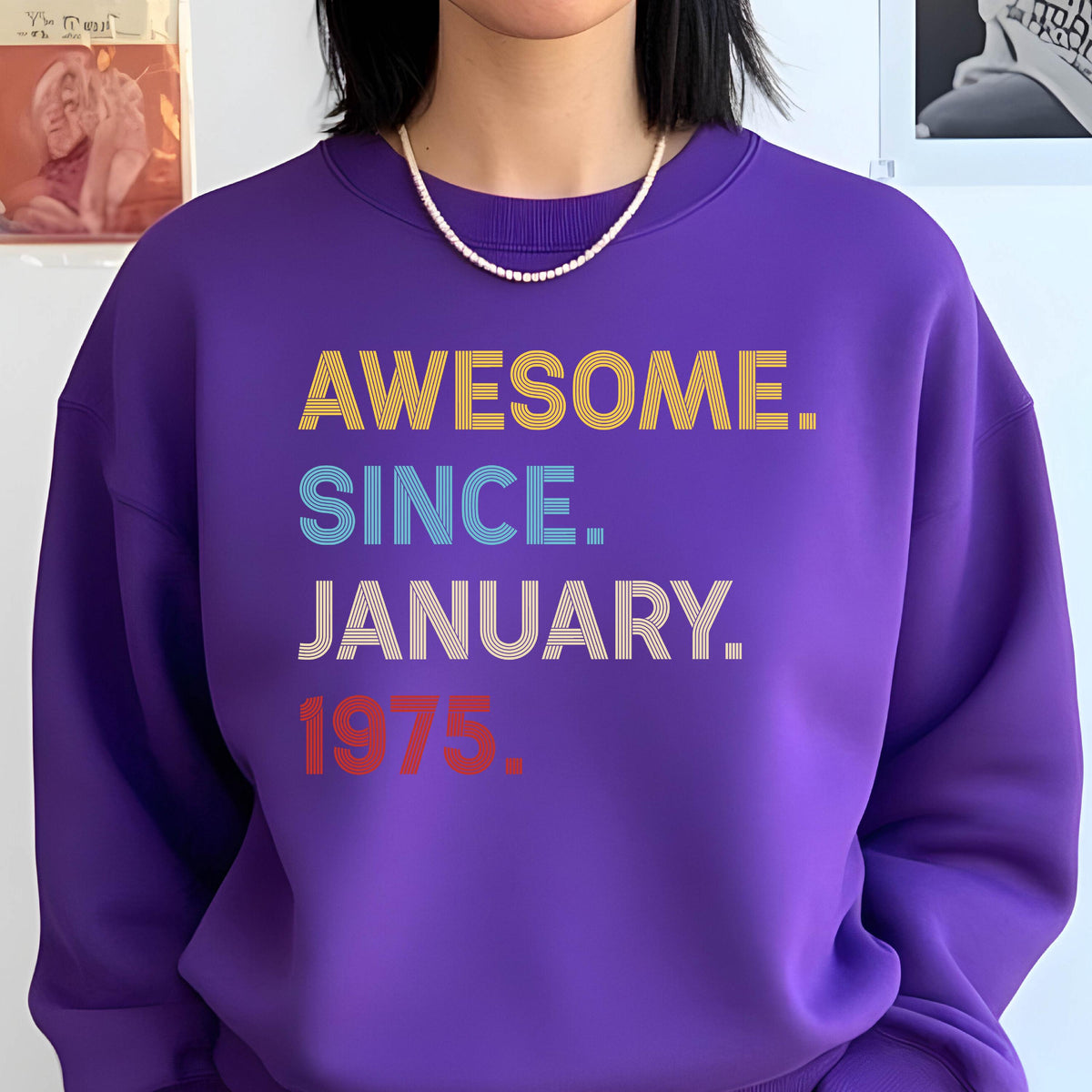 May include: A purple sweatshirt with the text "AWESOME. SINCE. JANUARY. 1975." in yellow, blue, white, and red. The sweatshirt is a solid color and has a crew neck.