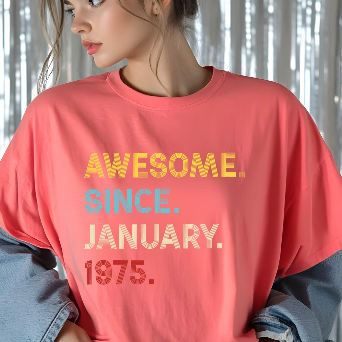 May include: A coral-colored crew neck t-shirt featuring the text AWESOME. SINCE. JANUARY. 1975. printed in a stacked, multi-colored striped font. The word AWESOME is yellow, SINCE is light blue, JANUARY is beige, and 1975 is red.