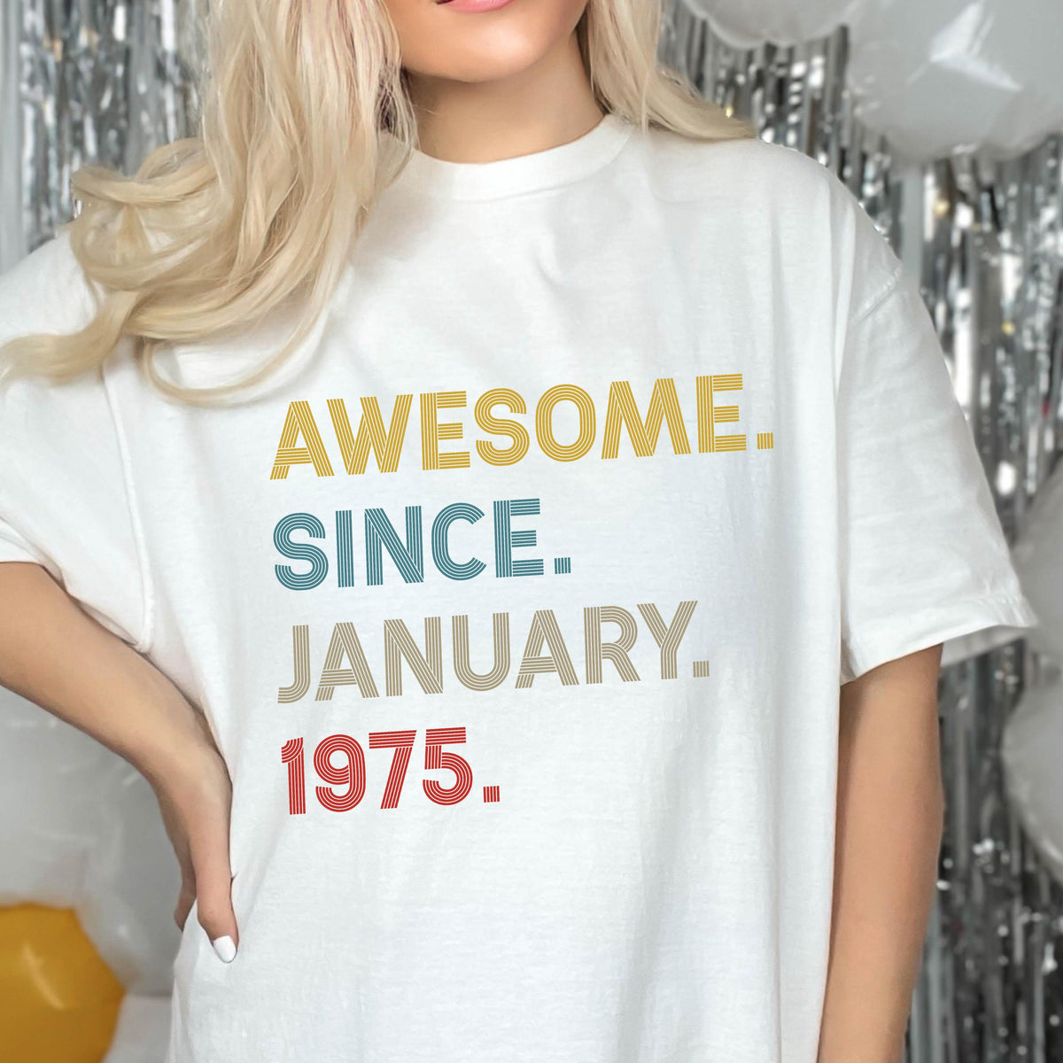 May include: A white short-sleeved t-shirt featuring the text AWESOME. SINCE. JANUARY. 1975. printed in a stacked layout. The word AWESOME is in yellow, SINCE is in blue, JANUARY is in beige, and 1975 is in red, all with a striped texture.