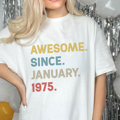 May include: A white short-sleeved t-shirt featuring the text AWESOME. SINCE. JANUARY. 1975. printed in a stacked layout. The word AWESOME is in yellow, SINCE is in blue, JANUARY is in beige, and 1975 is in red, all with a striped texture.