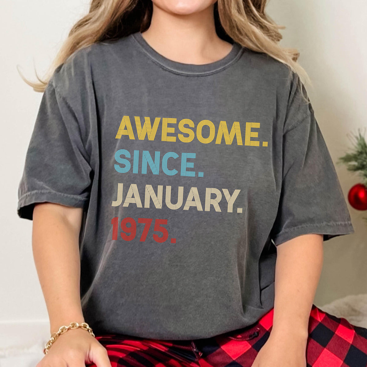 May include: A charcoal gray short-sleeve t-shirt featuring the text AWESOME. SINCE. JANUARY. 1975. The word AWESOME is in yellow, SINCE is in light blue, JANUARY is in white, and 1975 is in red, all displayed in a bold, sans-serif font.